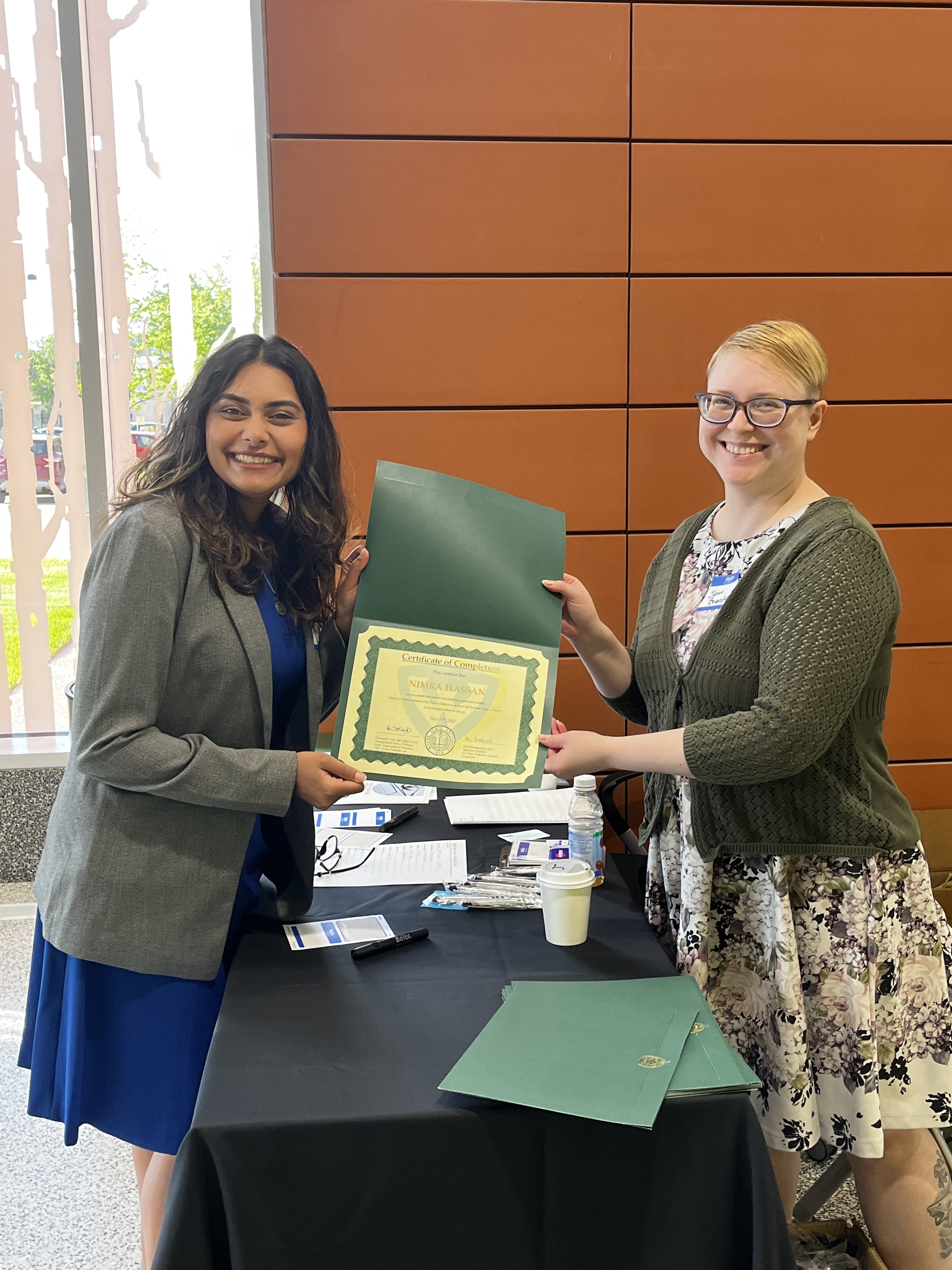 Nimra Hassan, graduating 2024 with an MPH, left, receives her certificate of completion from Jenn Brandt, Dept. of Pediatrics Secretary, right, at the 2023 Pediatric Research Day.
