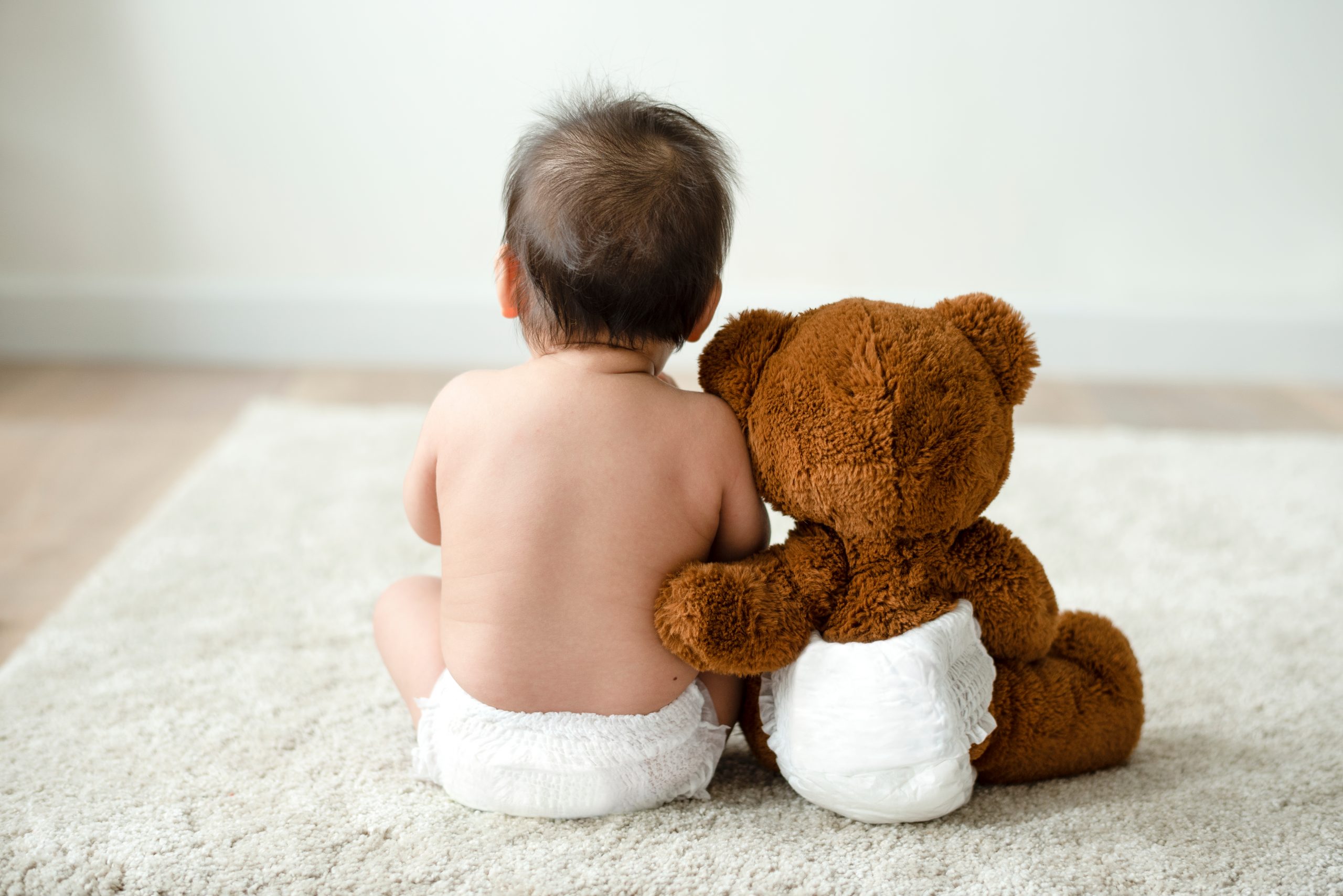 Baby in diaper sitting next to stuffed bear