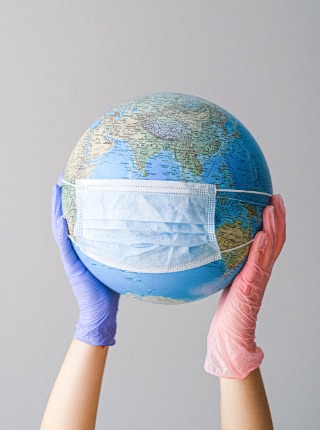 Two gloved hands holding a globe with a doctors mask pulled across